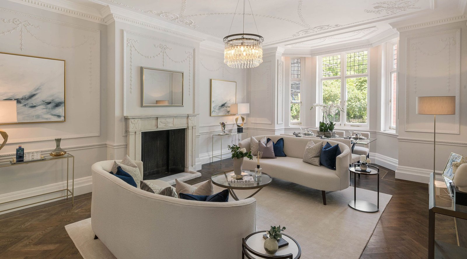 A bright and spacious living room in a restored London period property, featuring contemporary white sofas, a modern chandelier, and ornate original cornicing.
