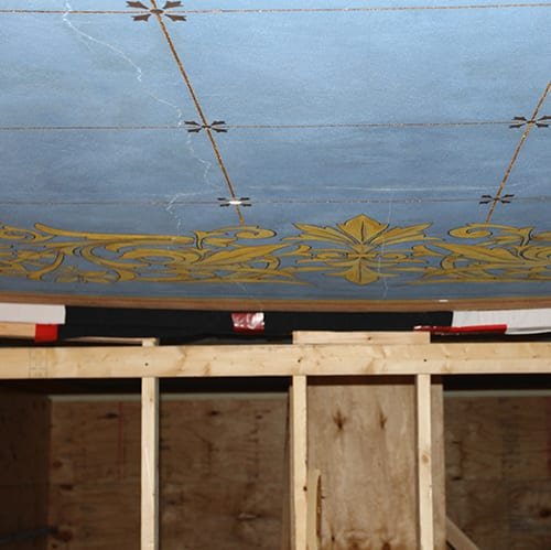 A skilled craftsman carefully restores the intricate details of a damaged plaster cornice in a heritage property.